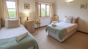A bedroom with two beds, a nightstand with a lamp, a chair, and a window with curtains.