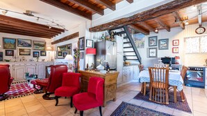 A spacious living room with red chairs, a wooden desk, and a dining area with a table and chairs. There is a kitchen area with a stove and refrigerator. - Casa Ultima - Superbe vue, proche Ajaccio (Sarrola-Carcopino)