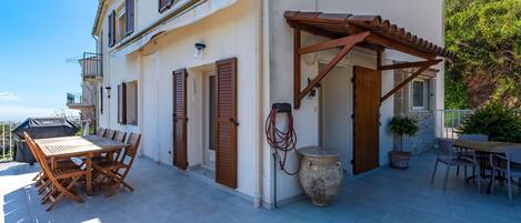 Un edificio de dos pisos con un patio amoblado con muebles de madera y una pérgola.