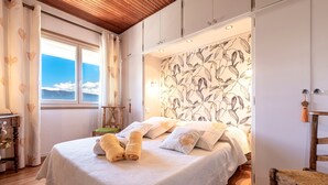 A bedroom with a bed, a window, and a wall with a floral pattern. - Casa Ultima - Superbe vue, proche Ajaccio (Sarrola-Carcopino)