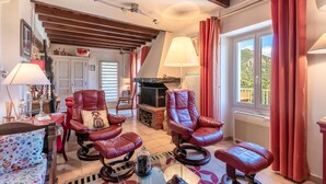 A cozy living room with leather sofas, a fireplace, and a large window with curtains. - Casa Ultima - Superbe vue, proche Ajaccio (Sarrola-Carcopino)