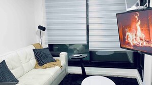 A modern living room with a white leather sofa, a black rug, a small round coffee table, a flat-screen TV, and a fireplace. - Luxury 1-bedroom apartment near WTC Montevideo with infinit pool (Montevideo)