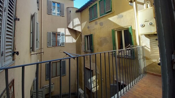 Une ruelle étroite bordée de bâtiments des deux côtés, avec des balcons dotés de garde-corps en métal et de volets.