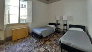 Une chambre avec deux lits, une commode et une fenêtre dont les volets sont ouverts.
