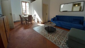 Un salon avec un canapé bleu, une table à manger avec des chaises, une petite table basse et un tapis à motifs.