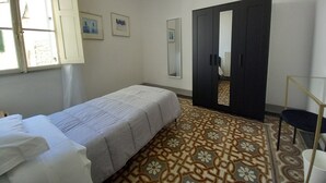 Une chambre d’hôtel avec un lit simple, un sol à motifs, une armoire, un miroir et une fenêtre avec des rideaux.