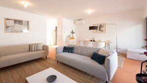 A modern living room with a sofa, coffee table, and a dining area with a table and chairs. - Villa Terracota by Acasadascasas (Mafra)