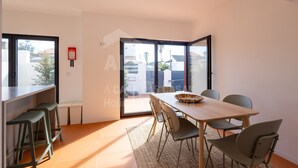A modern dining area with a wooden table, six chairs, and a large window with a view of buildings and trees. - Villa Terracota by Acasadascasas (Mafra)