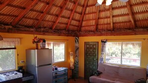 Una habitación acogedora con techo de paja, una kitchenette con refrigerador, una mesa de comedor y un sofá.