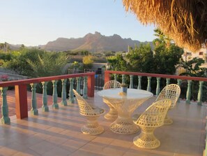 Une terrasse avec une table ronde et quatre chaises, une rambarde rouge et une vue sur les montagnes.