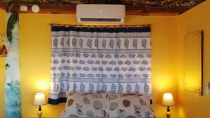 Una habitación con una cama, dos lámparas de noche, una cortina estampada, un equipo de aire acondicionado y una pared con un calendario.