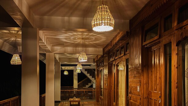 A wooden interior with a long corridor, hanging wicker chandeliers, and a staircase in the background. - The Woods - Tirthan Valley (Banjar)