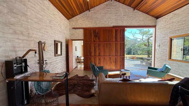 A cozy interior with a wooden ceiling, a large sliding door to a patio, a dining area, and a seating area with a sofa and chairs.