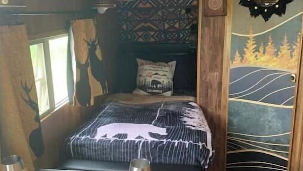 A cozy room with a bed, a table with a glass and a plate, and a patterned wall.