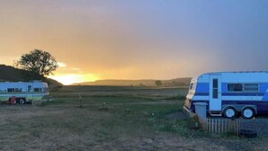 A campsite with two RVs parked on a grassy field during sunset.