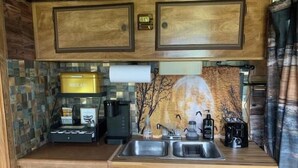 A compact kitchen with wooden cabinets, a coffee maker, and a small refrigerator.