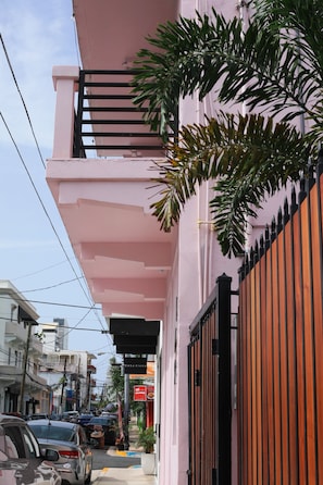 A pink building with a balcony, a gated entrance, and a street view with parked cars. - Room 10: Cozy Urban Hideaway in Arts District (San Juan)