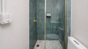 A glass-enclosed shower with a gold shower head, a white toilet, and a white sink. -  Room 10: Cozy Urban Hideaway in Arts District (San Juan)