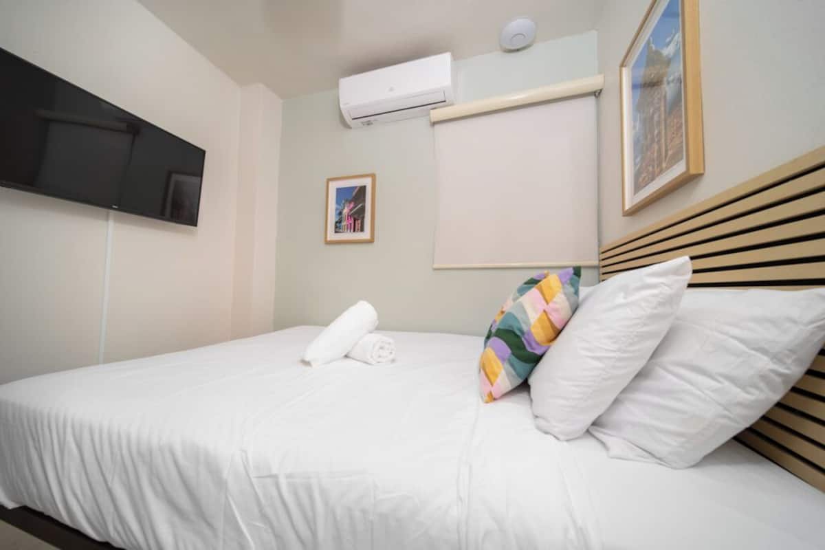 Habitación de hotel con cama, televisión de pantalla plana montada en la pared, equipo de aire acondicionado y un cuadro enmarcado.