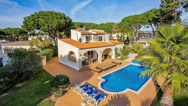 A two-story villa with a swimming pool, outdoor seating, and lush greenery.
