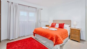 A hotel room with a bed, two bedside tables, a red rug, and a window with curtains.