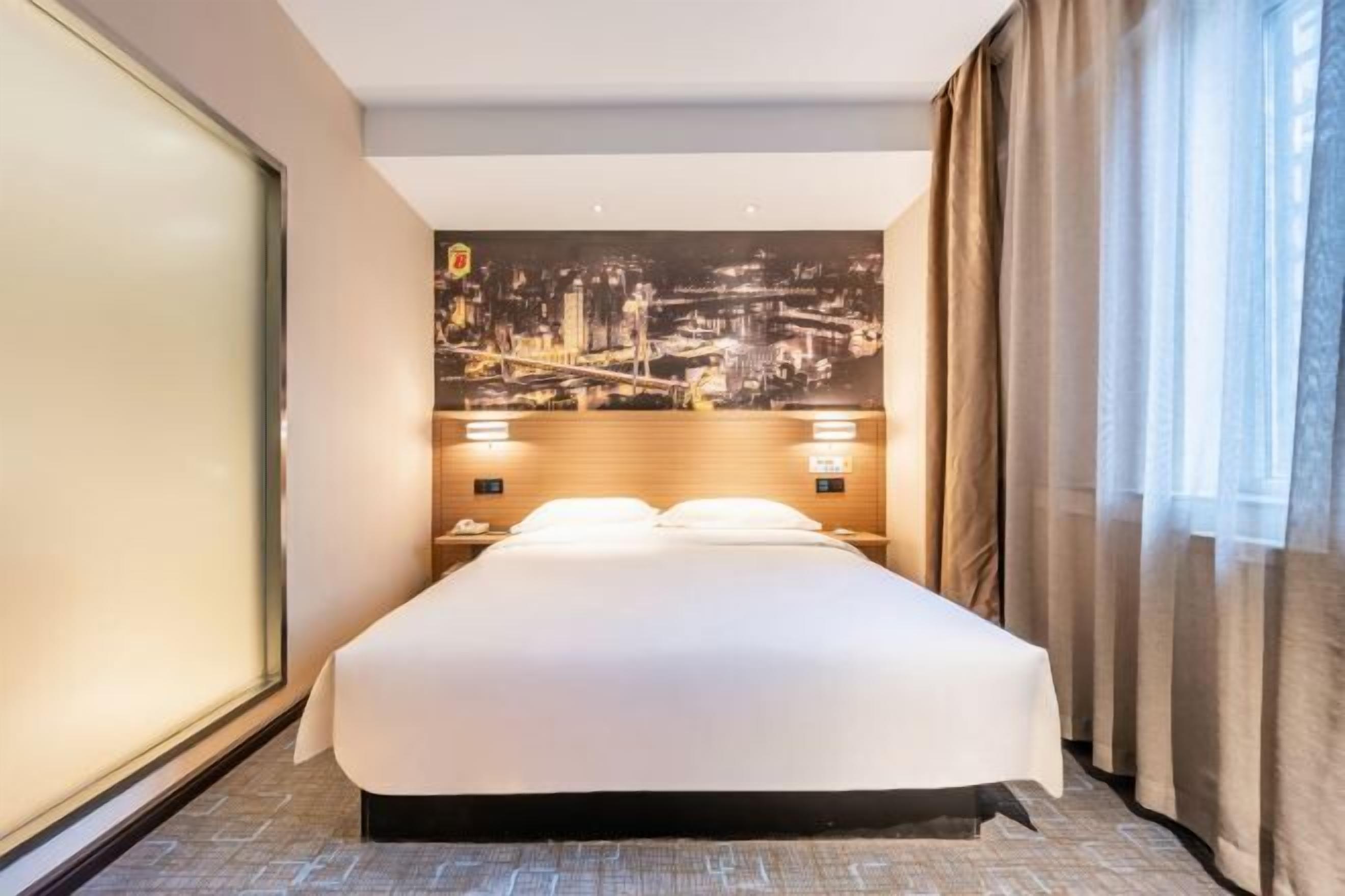 Habitación de hotel con una cama grande, un mural de paisaje urbano en la pared y una mesita de noche con un teléfono y una lámpara.
