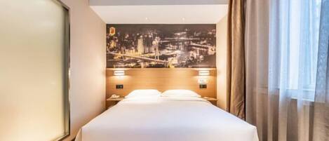 Habitación de hotel con una cama grande, un mural de paisaje urbano en la pared y una mesita de noche con un teléfono y una lámpara.
