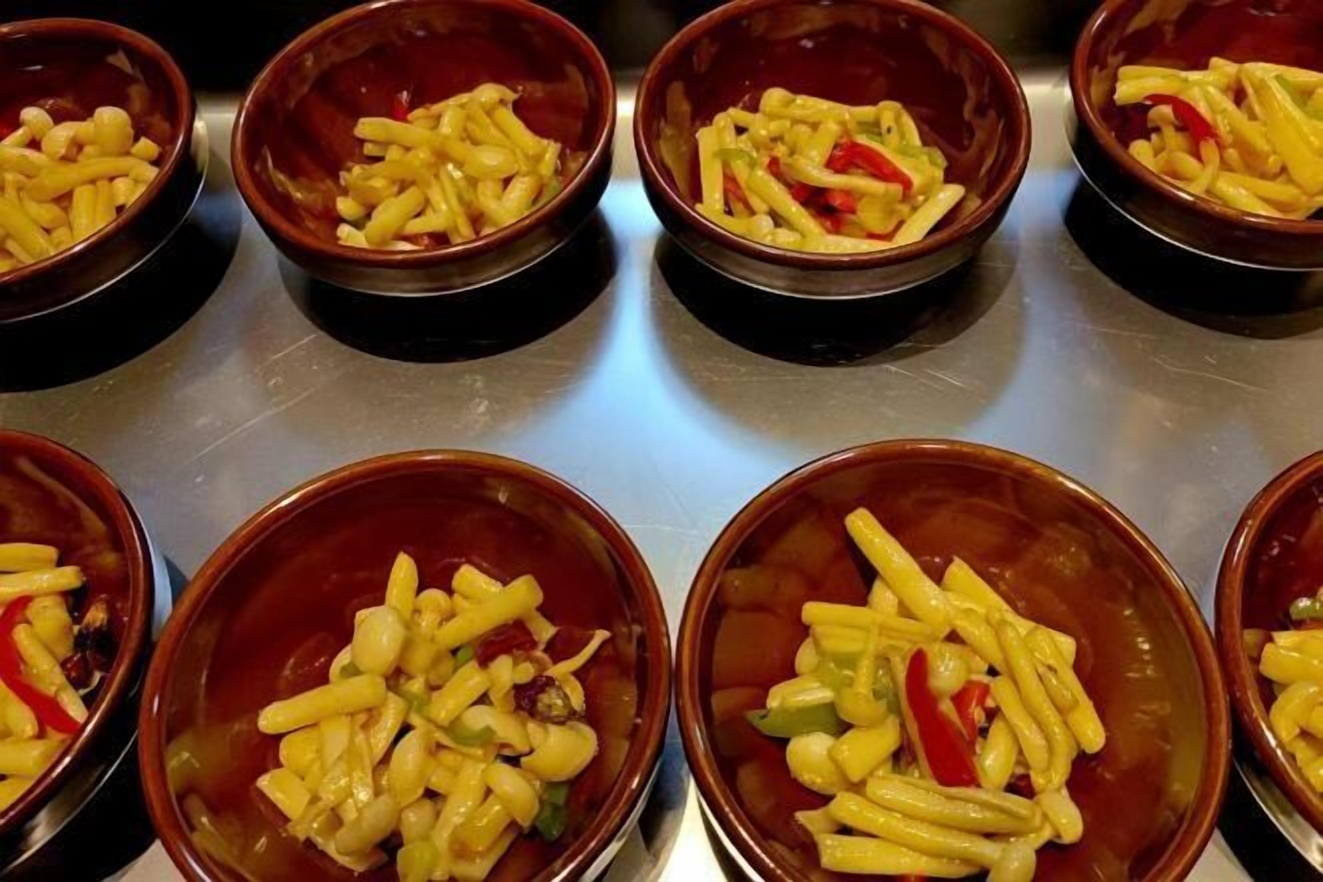 Multiple bowls of pasta with vegetables on a stainless steel surface.
