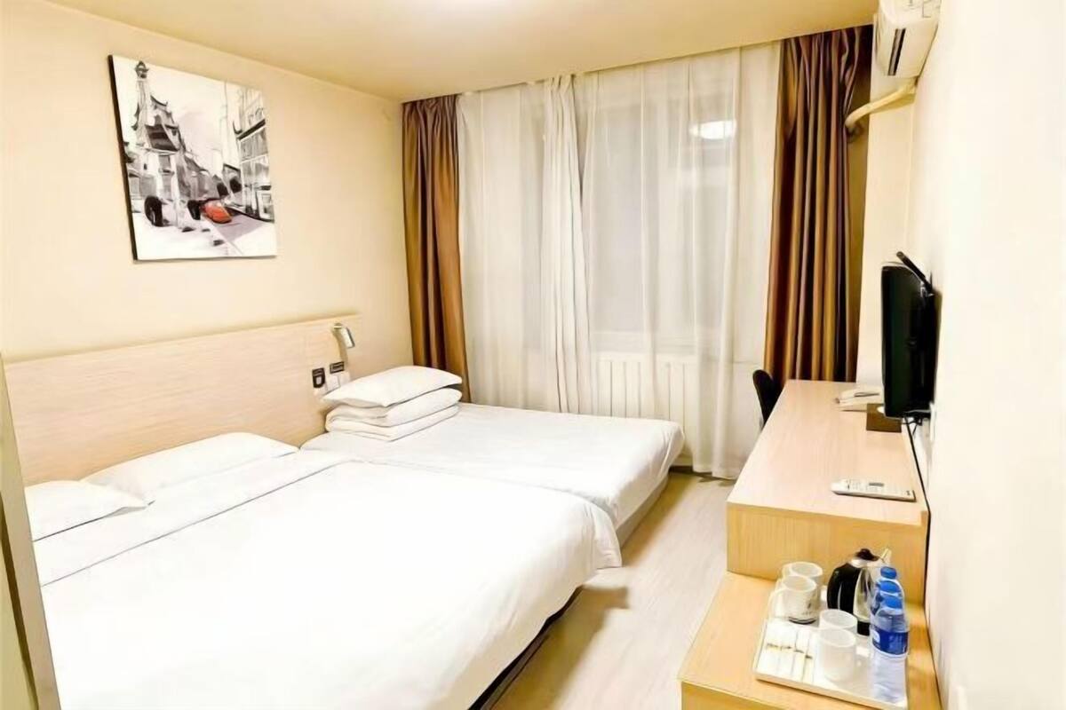 A hotel room with two beds, a desk with a chair, a television, and a window with curtains.