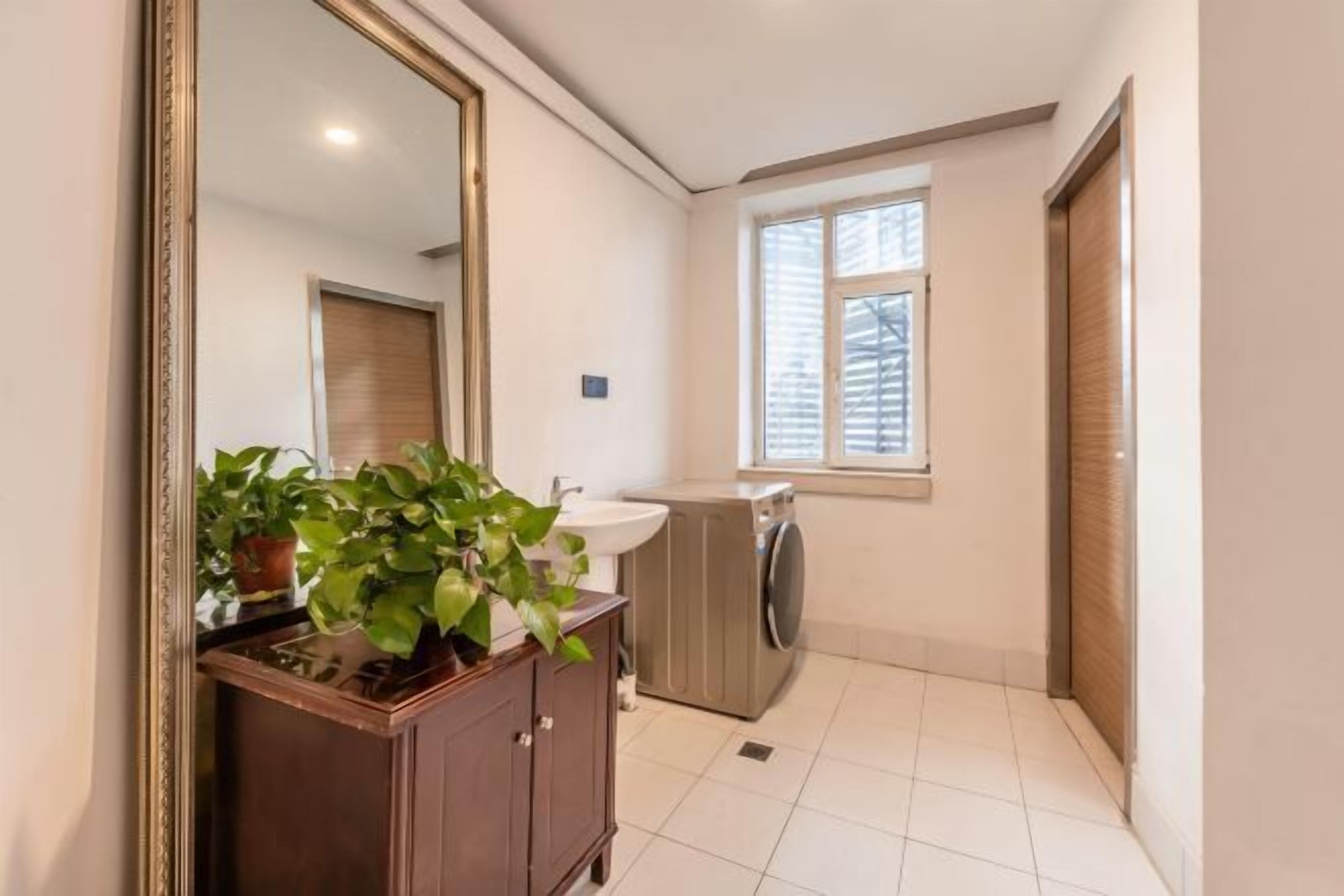 A compact bathroom with a wooden vanity, a sink, a washing machine, and a window with blinds.