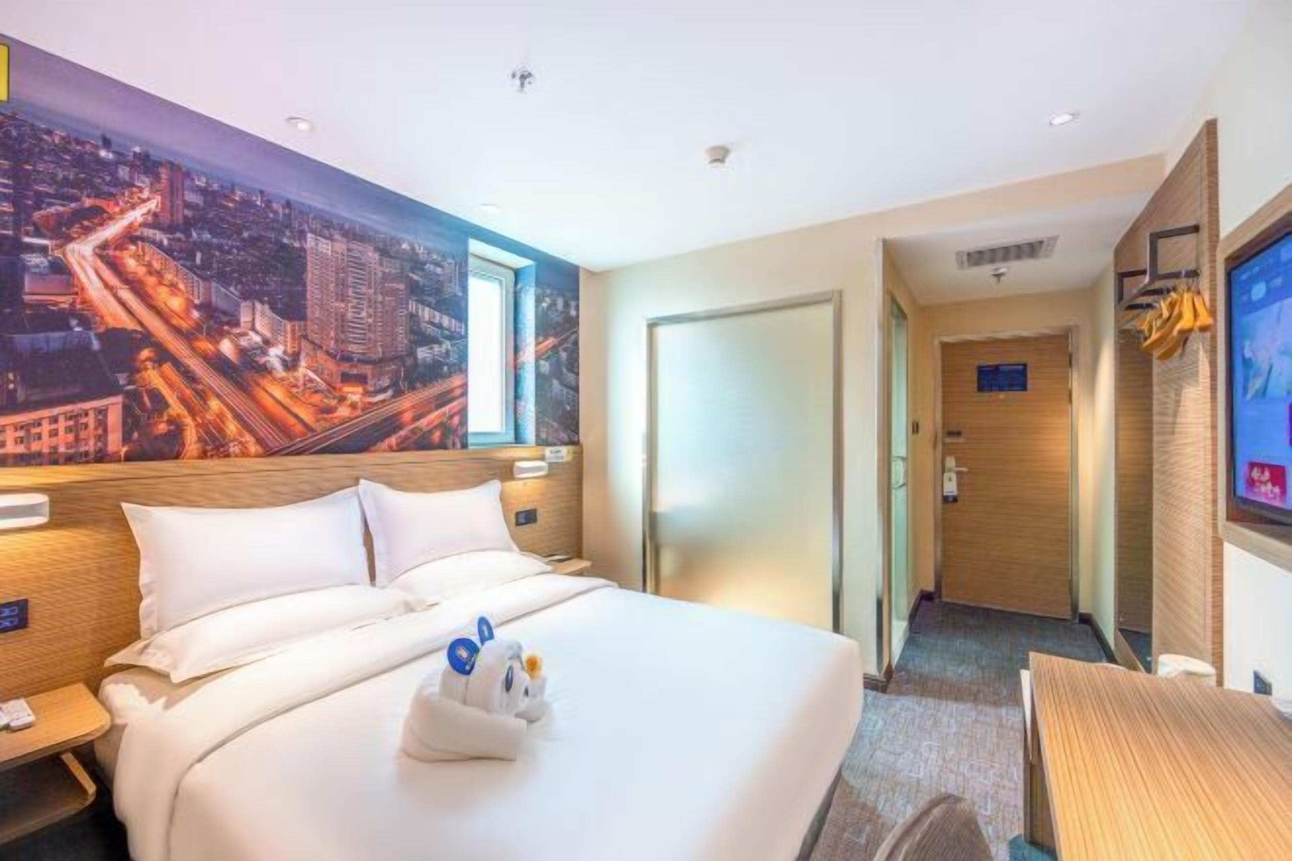 Una habitación de hotel con una cama grande, un mural de paisaje urbano en la pared, un escritorio y un televisor.