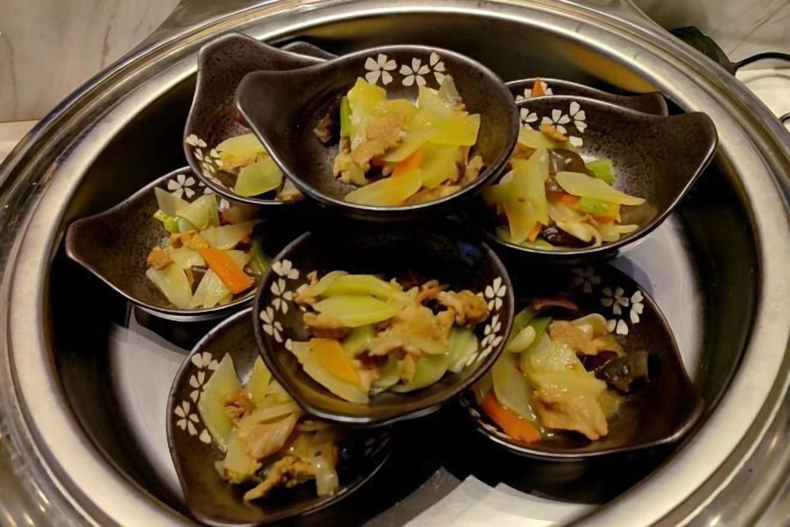 Een dienblad met meerdere kleine schaaltjes met een gerecht van groenten en vlees.