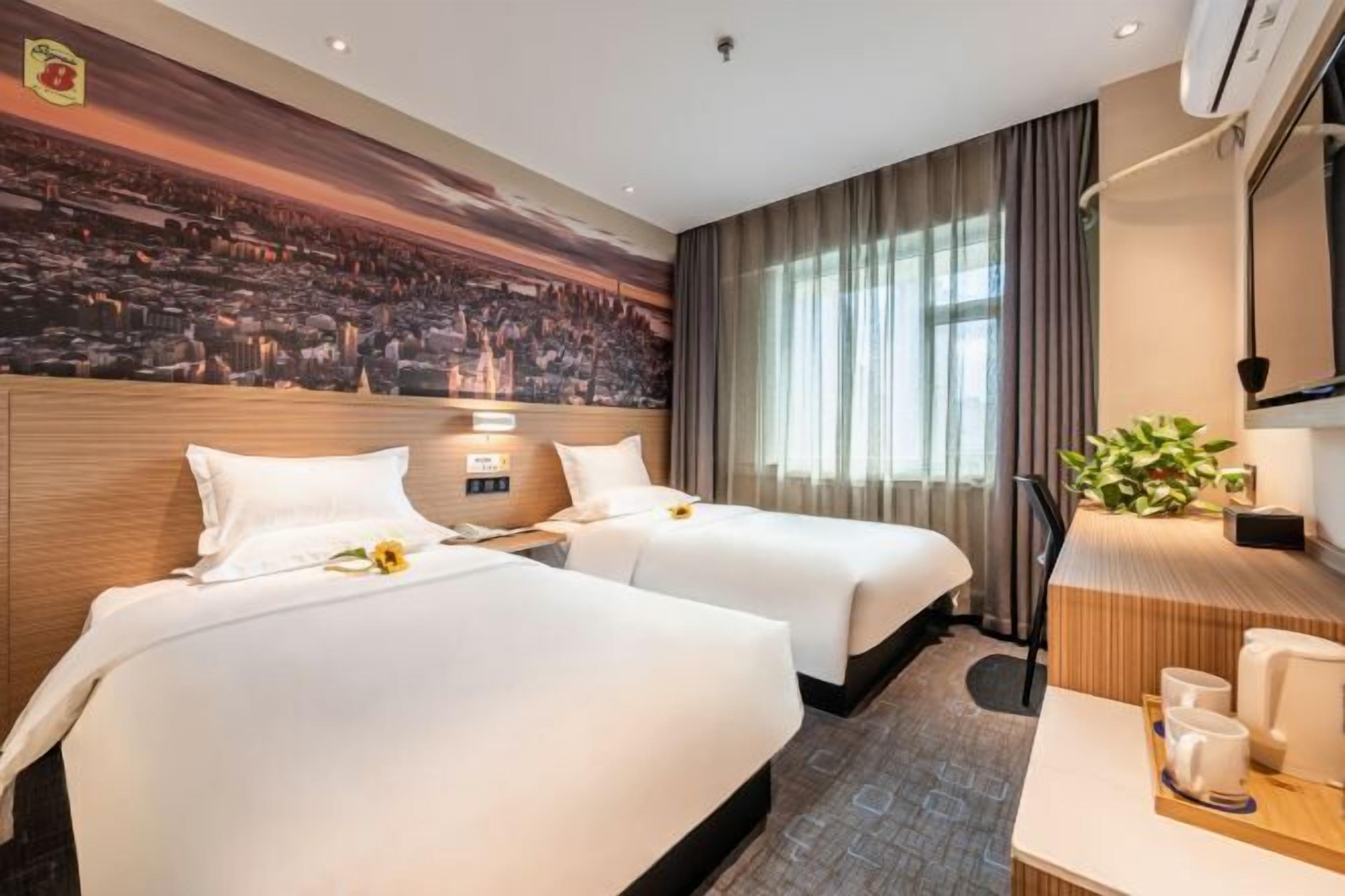Habitación de hotel con dos camas, un escritorio, una silla, un televisor y un mural grande en la pared.