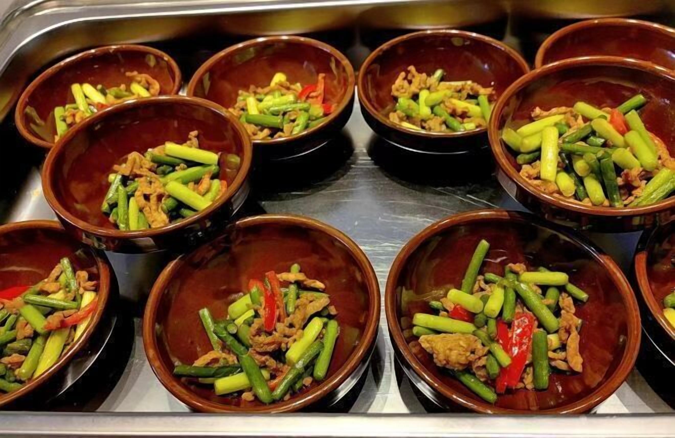 A stainless steel buffet line with multiple brown bowls containing stir-fried vegetables and meat.