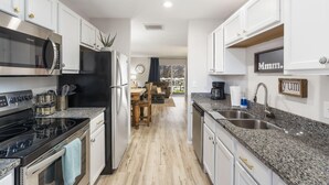 A modern kitchen with white cabinets, a black refrigerator, stainless steel appliances, granite countertops, and a dining area with a view. - 3BR Walk-In Condo | Spacious Deck | Sleeps 11 (Branson)