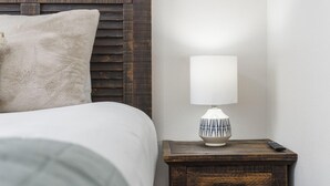 A neatly made bed with a white comforter and a fluffy pillow, a bedside table with a white lamp, and a remote control on the table. - 3BR Walk-In Condo | Spacious Deck | Sleeps 11 (Branson)
