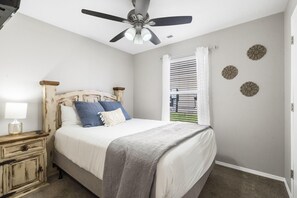 Une chambre à coucher comprenant un lit, une table de chevet, un ventilateur de plafond et des œuvres d’art décoratives murales.