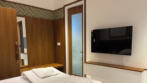 A hotel room with a bed, a TV mounted on the wall, a wooden wardrobe, and a mirror. - The Old City (Kanchipuram)