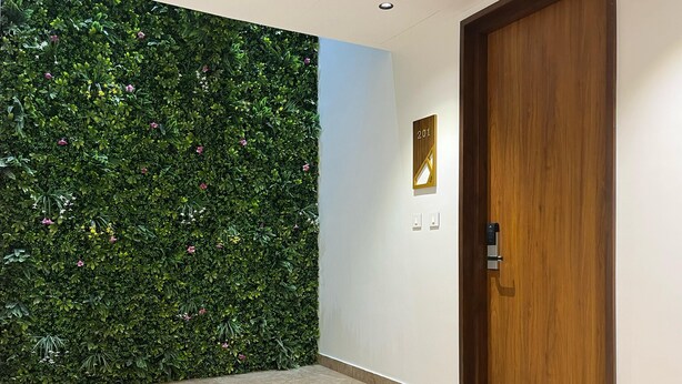 A hallway with a green wall covered in plants and flowers, a wooden door, and a number sign. - The Old City (Kanchipuram)
