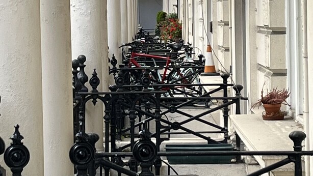 Ein Korridor mit weißen Säulen, einem Fahrradständer mit Fahrrädern und einem Blumentopf.