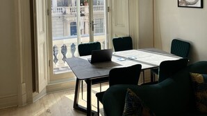 Ein Zimmer mit großem Fenster, einem Tisch mit Stühlen, einer Couch und einem gerahmten Bild an der Wand.