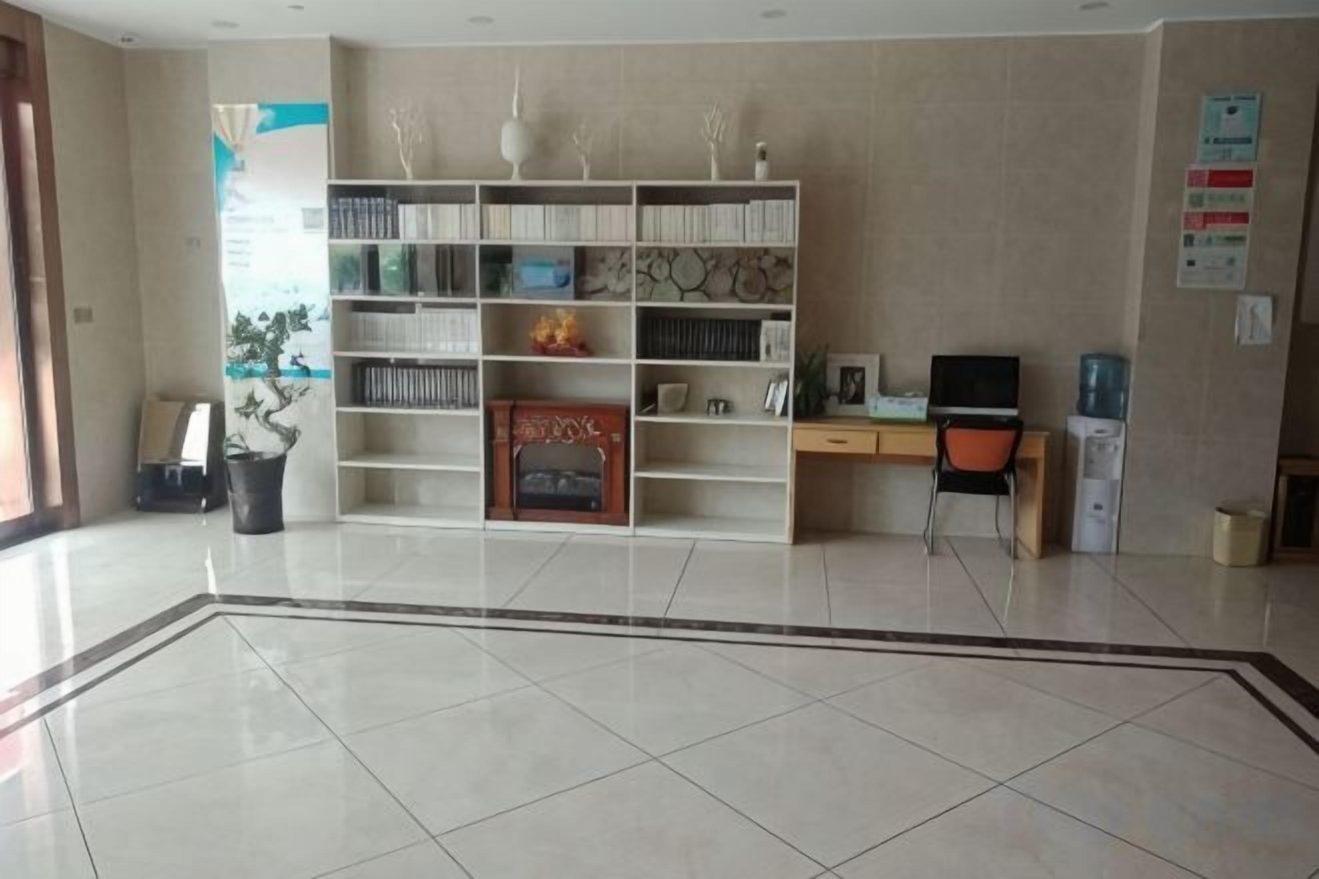 A reception area with a tiled floor, a reception desk, a bookshelf, and a potted plant.