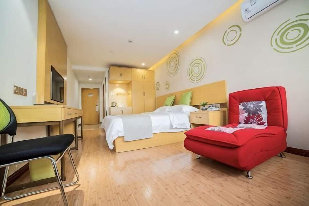 A hotel room with a bed, a desk, a chair, and a red sofa.