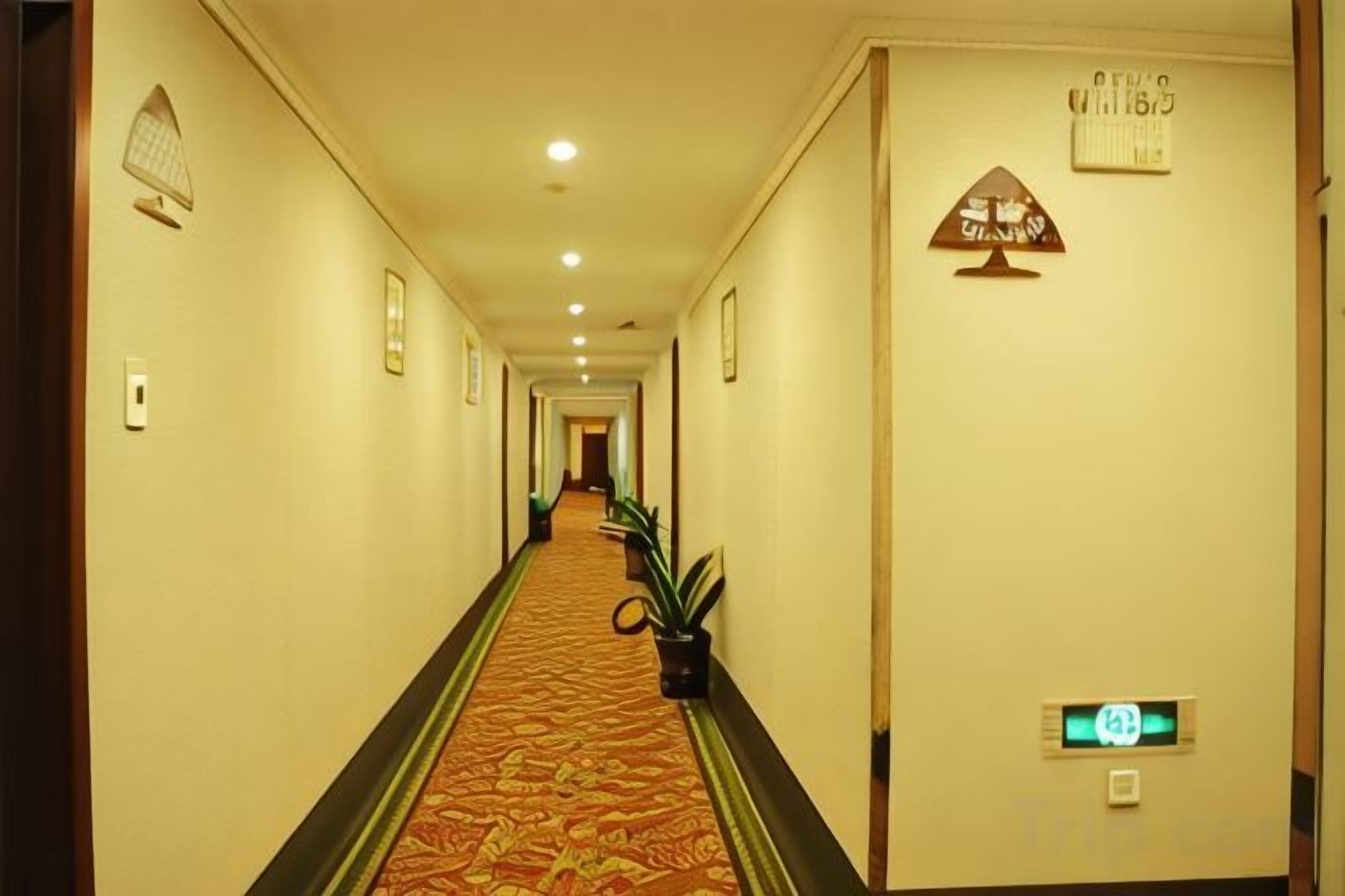 Un pasillo de hotel con piso alfombrado, un mostrador de recepción y una señal que indica el camino a los ascensores.