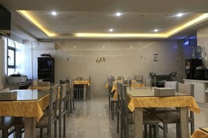 Un restaurante con varias mesas y sillas, una zona de cocina y una barra con una máquina de café.