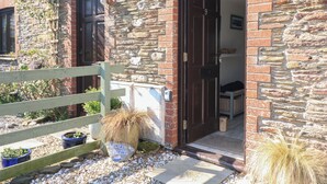 A stone building with a wooden fence, a door, and potted plants. - Tinkers Cottage (Kingsbridge)