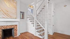 A spacious room with a wooden floor, a white staircase, and a fireplace.