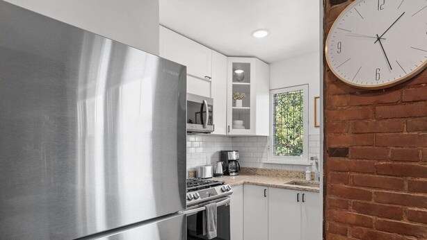 A modern kitchen with stainless steel appliances, white cabinetry, and a brick wall.