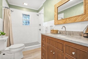 A bathroom with a shower, toilet, vanity, and a mirror.