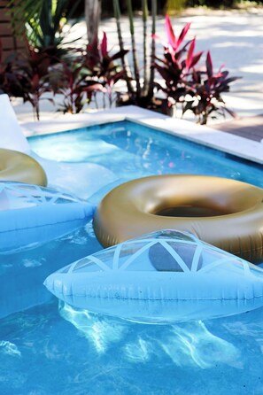 A swimming pool with inflatable rings and plants in the background.